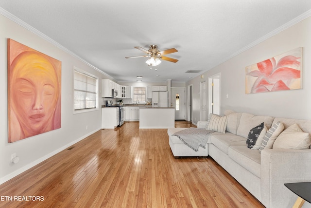 living room featuring ceiling fan, light wood-type flooring, ornamental molding, and sink