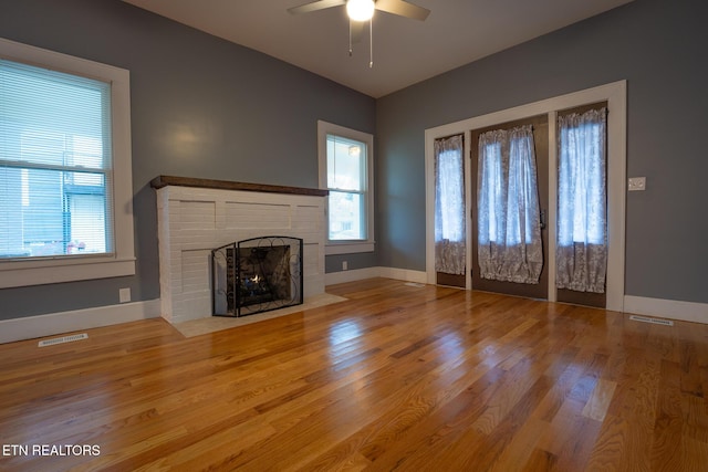 unfurnished living room featuring a brick fireplace, a healthy amount of sunlight, hardwood / wood-style floors, and ceiling fan