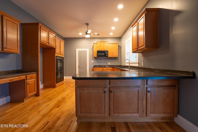 kitchen featuring sink, built in desk, black appliances, kitchen peninsula, and light wood-type flooring