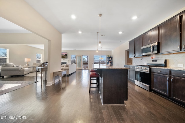 kitchen featuring a breakfast bar area, stainless steel appliances, decorative backsplash, a kitchen island with sink, and light stone counters