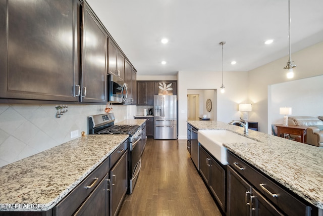 kitchen featuring a center island with sink, appliances with stainless steel finishes, tasteful backsplash, pendant lighting, and light stone counters