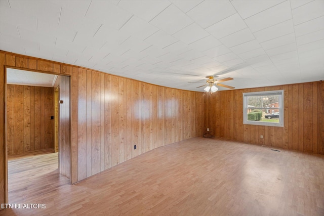 unfurnished room with ceiling fan, wood walls, and light wood-type flooring