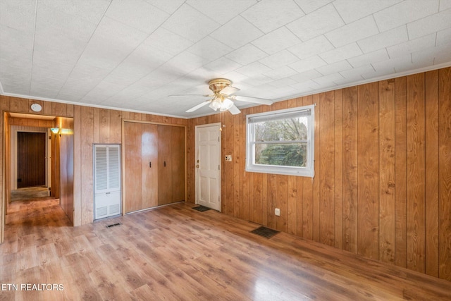 unfurnished bedroom with hardwood / wood-style flooring, ceiling fan, and wooden walls