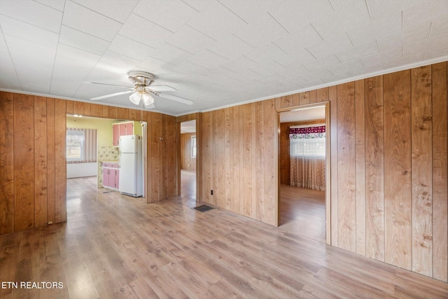 spare room with light wood-type flooring, ceiling fan, and wooden walls