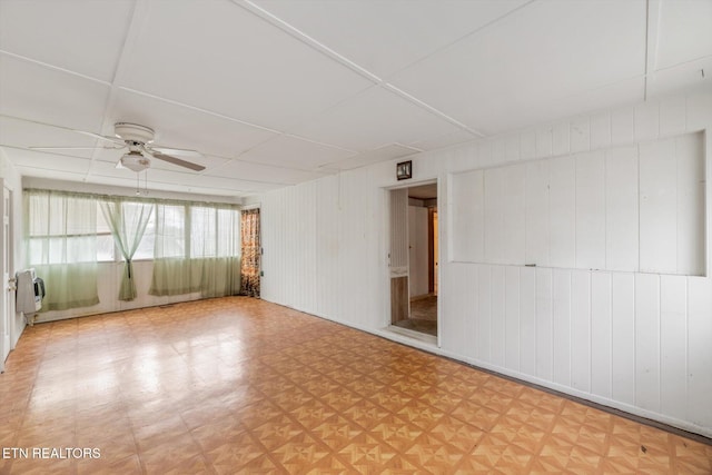 empty room featuring heating unit, wooden walls, and ceiling fan