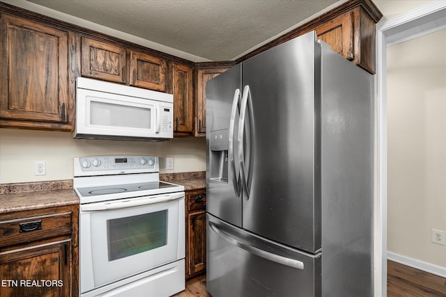 kitchen with a textured ceiling, white appliances, and dark wood-type flooring