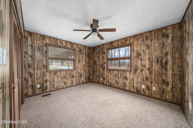 unfurnished room featuring ceiling fan, wood walls, and carpet floors