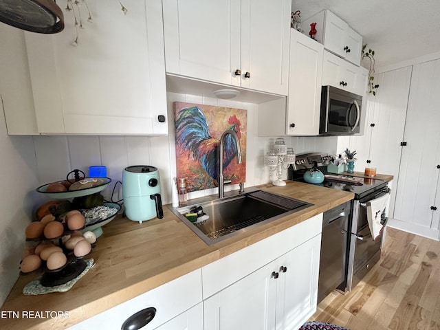 kitchen featuring butcher block counters, sink, light hardwood / wood-style flooring, white cabinets, and appliances with stainless steel finishes