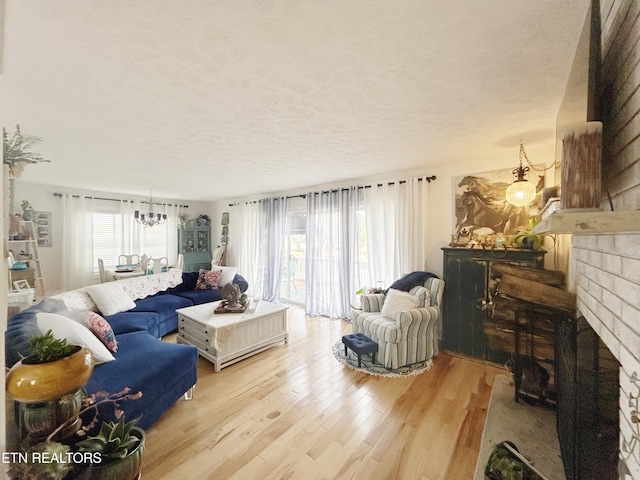 living room featuring a chandelier, a textured ceiling, light hardwood / wood-style floors, and a brick fireplace