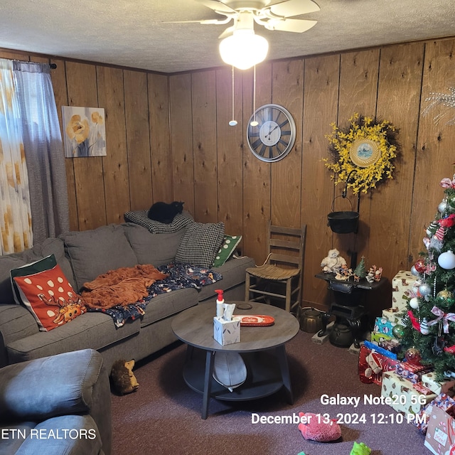 living room featuring carpet, a textured ceiling, ceiling fan, and wooden walls