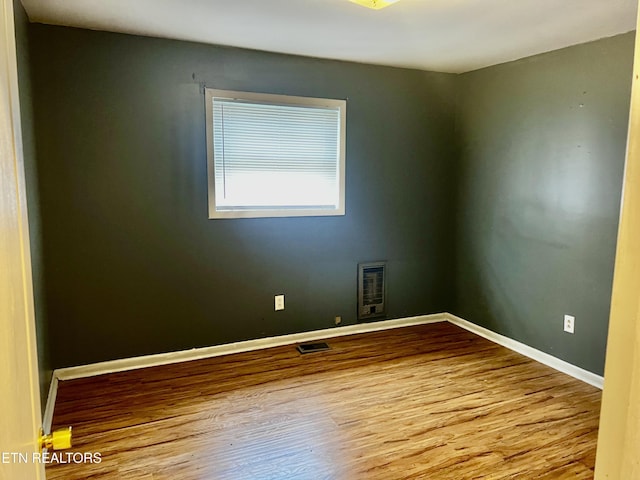 unfurnished room featuring heating unit and hardwood / wood-style floors