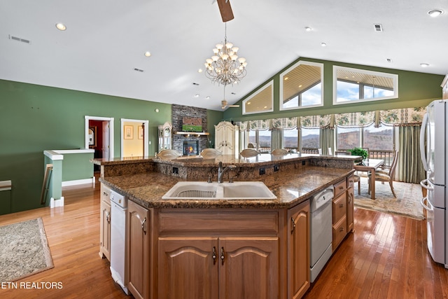 kitchen with stainless steel appliances, a kitchen island with sink, sink, wood-type flooring, and hanging light fixtures