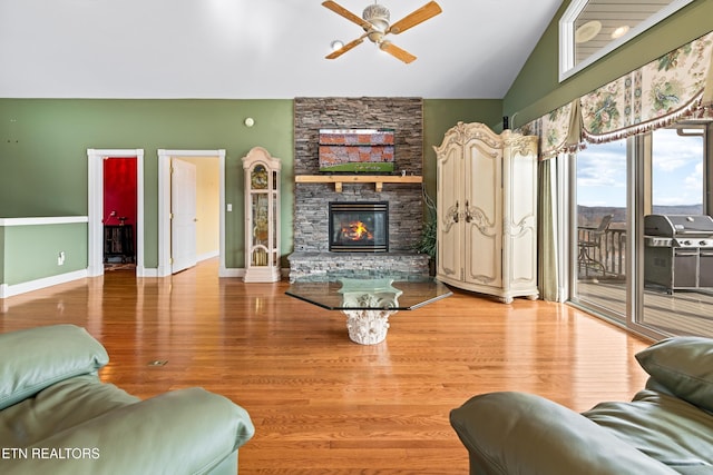 living room featuring hardwood / wood-style floors, a stone fireplace, ceiling fan, and lofted ceiling