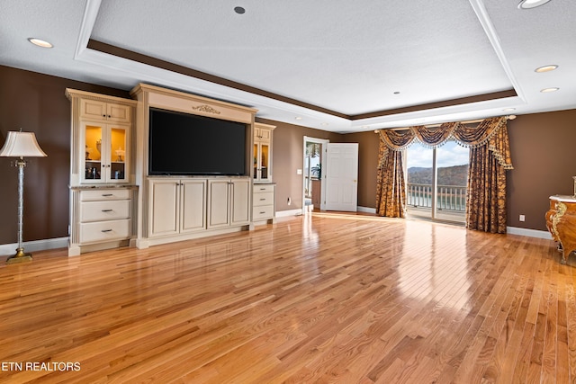 unfurnished living room with a textured ceiling, light wood-type flooring, and a raised ceiling