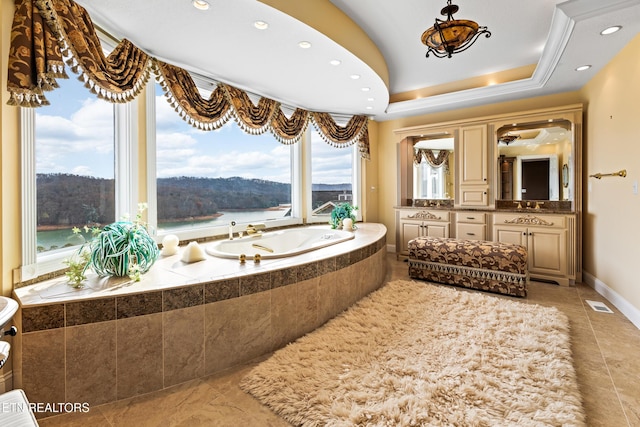 bathroom featuring vanity, a tray ceiling, crown molding, a water view, and a relaxing tiled tub