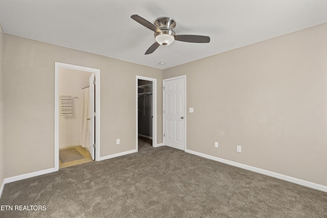 unfurnished bedroom featuring a spacious closet, dark carpet, ceiling fan, connected bathroom, and a closet