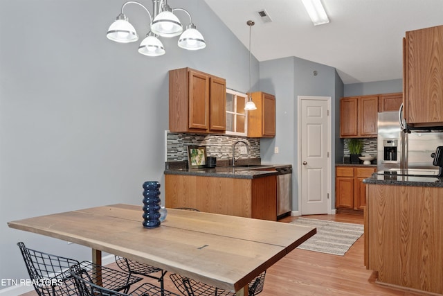 kitchen featuring appliances with stainless steel finishes, lofted ceiling, decorative light fixtures, sink, and backsplash