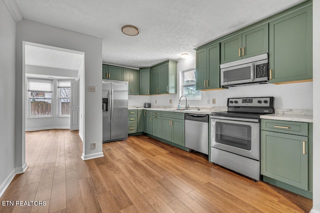 kitchen with green cabinets, stainless steel appliances, and light wood-type flooring