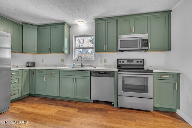 kitchen with green cabinets, sink, a textured ceiling, light hardwood / wood-style floors, and stainless steel appliances