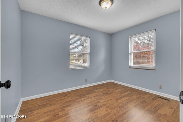 spare room featuring hardwood / wood-style floors, a textured ceiling, and a wealth of natural light