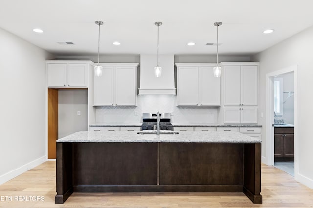 kitchen with white cabinets, light wood-type flooring, sink, and an island with sink