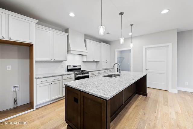 kitchen with gas range, light hardwood / wood-style floors, decorative light fixtures, white cabinets, and custom range hood