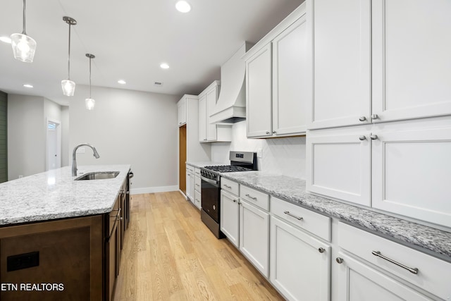 kitchen with gas range, sink, decorative light fixtures, white cabinets, and light hardwood / wood-style floors