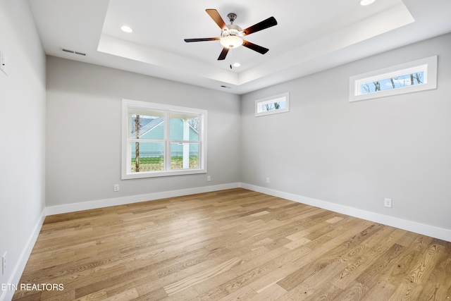 spare room featuring ceiling fan, a tray ceiling, and light hardwood / wood-style flooring