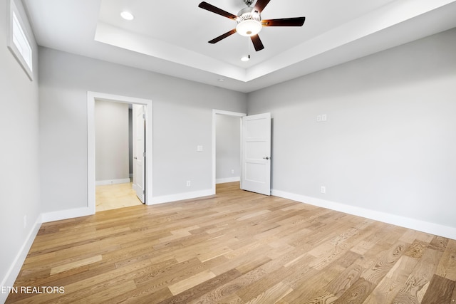 unfurnished bedroom with a tray ceiling, light hardwood / wood-style flooring, and ceiling fan