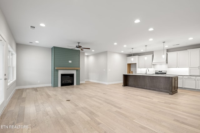 unfurnished living room featuring ceiling fan, sink, light wood-type flooring, and a fireplace