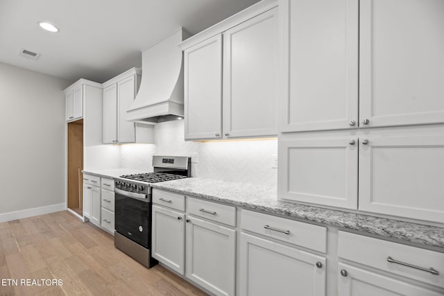 kitchen with gas stove, light stone countertops, custom range hood, and white cabinetry