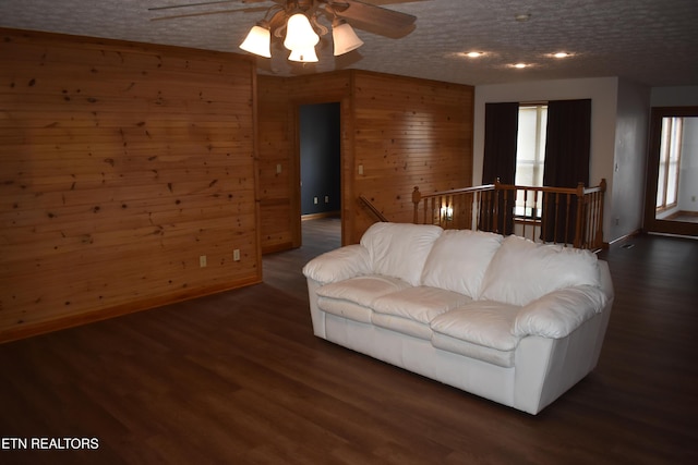 living room with wooden walls, ceiling fan, dark wood-type flooring, and a textured ceiling