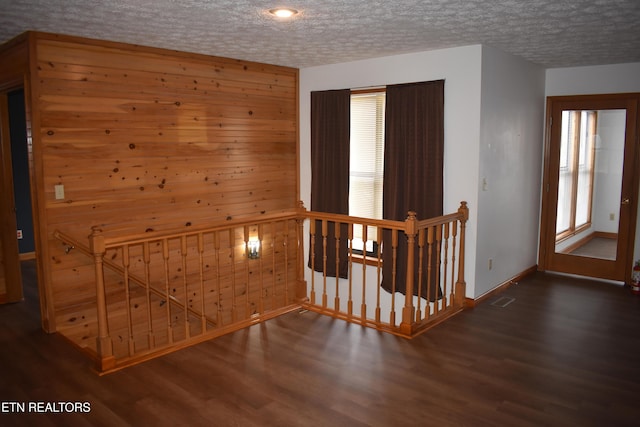 hallway featuring a textured ceiling, wood walls, and dark wood-type flooring