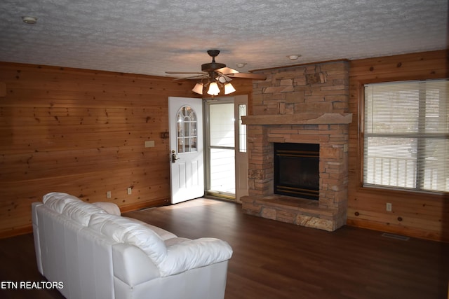 living room featuring a textured ceiling, ceiling fan, wooden walls, dark wood-type flooring, and a fireplace