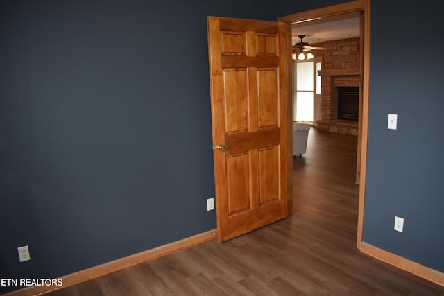 empty room with a stone fireplace, ceiling fan, and dark hardwood / wood-style floors