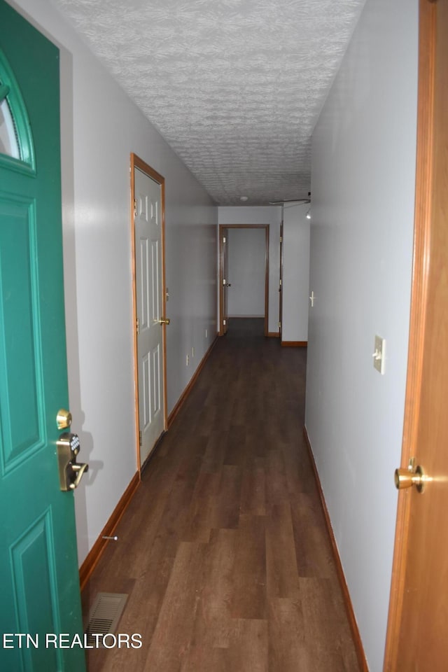 corridor with a textured ceiling and dark hardwood / wood-style floors