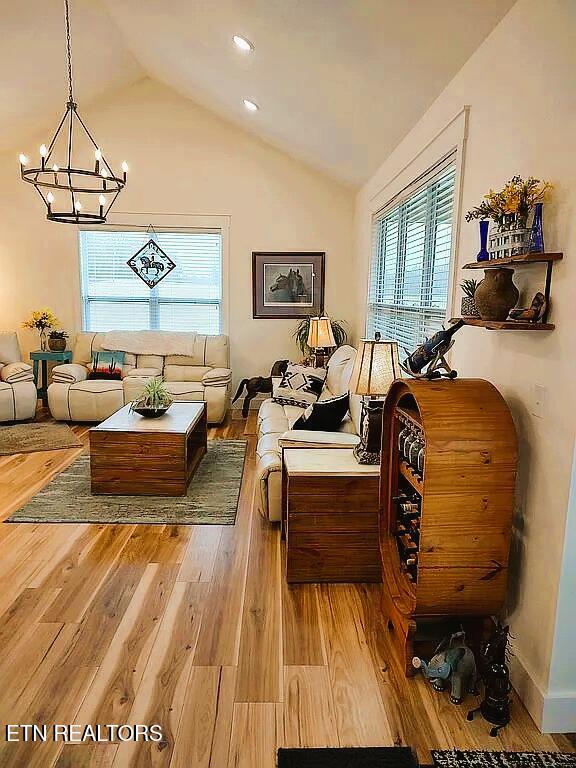 living area with wood-type flooring, a healthy amount of sunlight, vaulted ceiling, and a notable chandelier