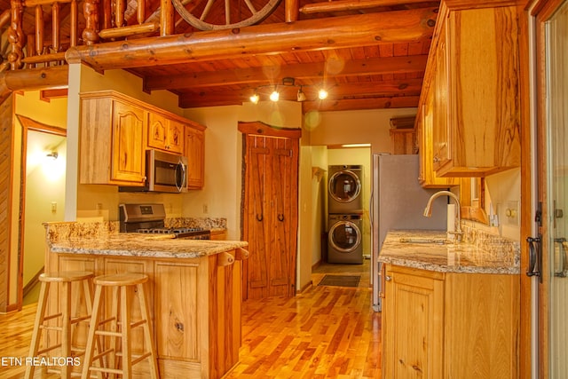 kitchen with appliances with stainless steel finishes, wood ceiling, a breakfast bar, beamed ceiling, and stacked washer / drying machine