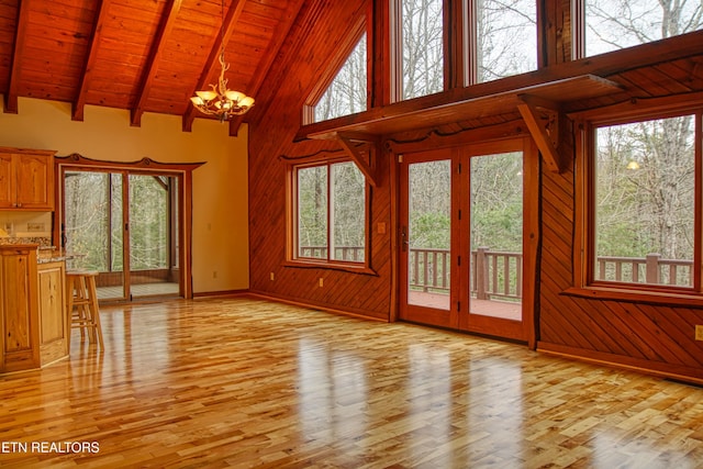 unfurnished living room with beam ceiling, wooden walls, wood ceiling, and a notable chandelier