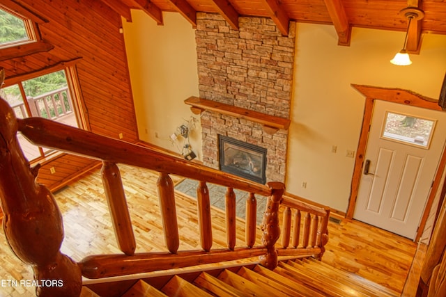 stairs featuring a stone fireplace, hardwood / wood-style floors, beamed ceiling, and wood ceiling