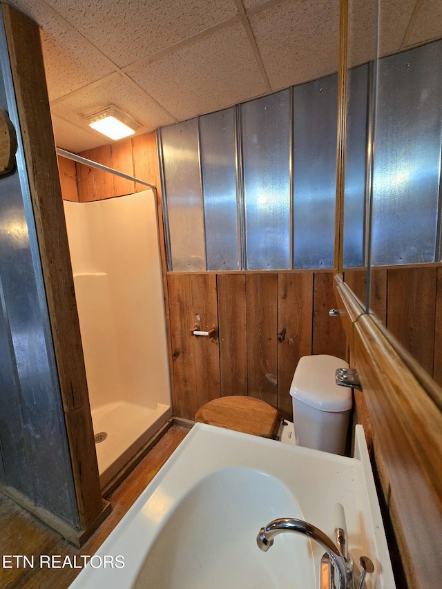 bathroom with a paneled ceiling, wood walls, sink, and a shower