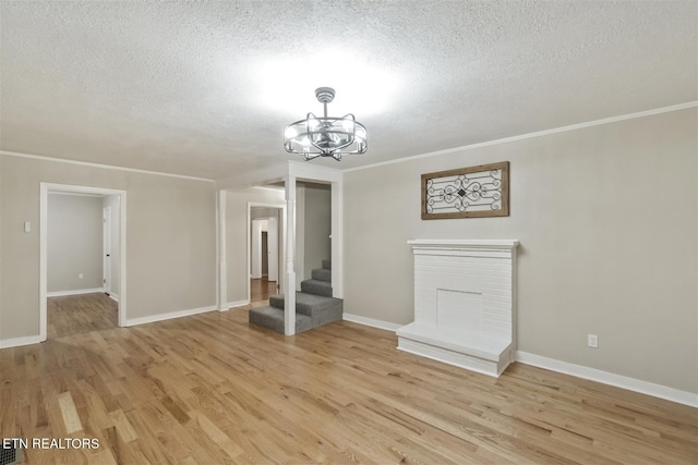 unfurnished living room with crown molding, light hardwood / wood-style flooring, a chandelier, and a textured ceiling