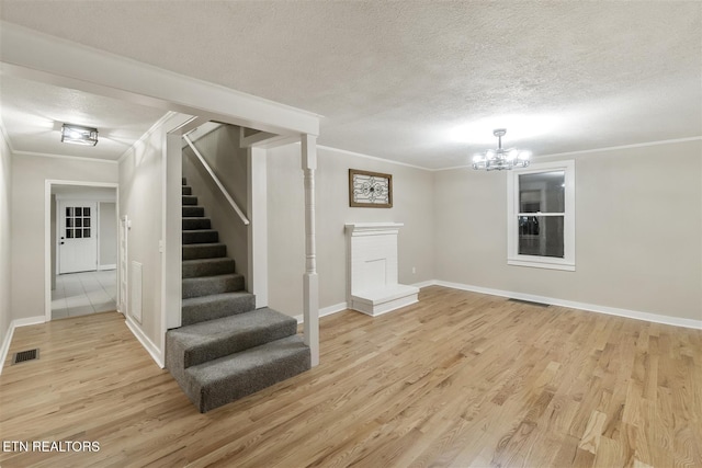 basement with a chandelier, a textured ceiling, light hardwood / wood-style flooring, and crown molding