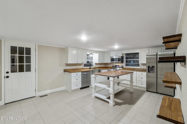 kitchen with wood counters, light tile patterned floors, white cabinetry, and appliances with stainless steel finishes