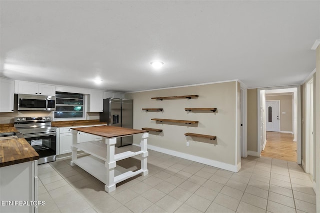 kitchen featuring butcher block countertops, white cabinetry, light tile patterned floors, and stainless steel appliances