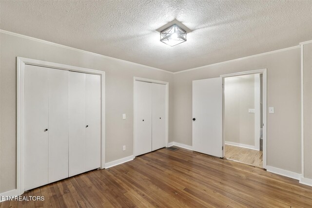 unfurnished bedroom with wood-type flooring, a textured ceiling, and ornamental molding