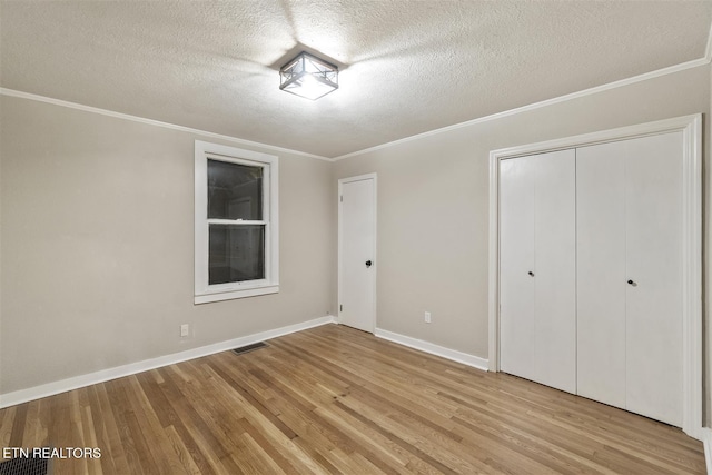 unfurnished bedroom featuring light hardwood / wood-style floors, ornamental molding, a textured ceiling, and a closet