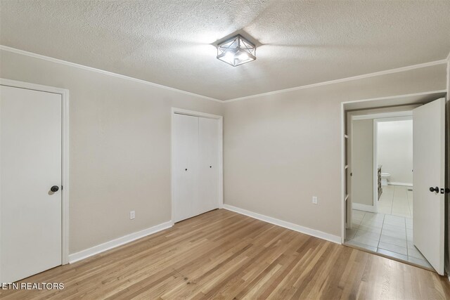 unfurnished bedroom featuring ornamental molding, light wood-type flooring, a textured ceiling, and a closet