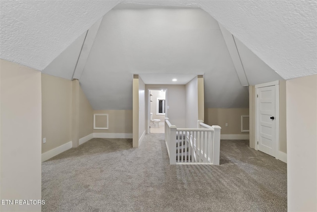 bonus room with vaulted ceiling, light colored carpet, and a textured ceiling