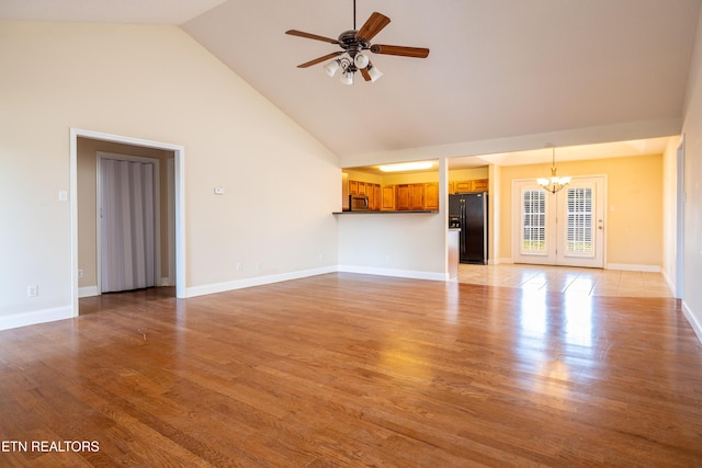 unfurnished living room with ceiling fan with notable chandelier, light hardwood / wood-style floors, and high vaulted ceiling